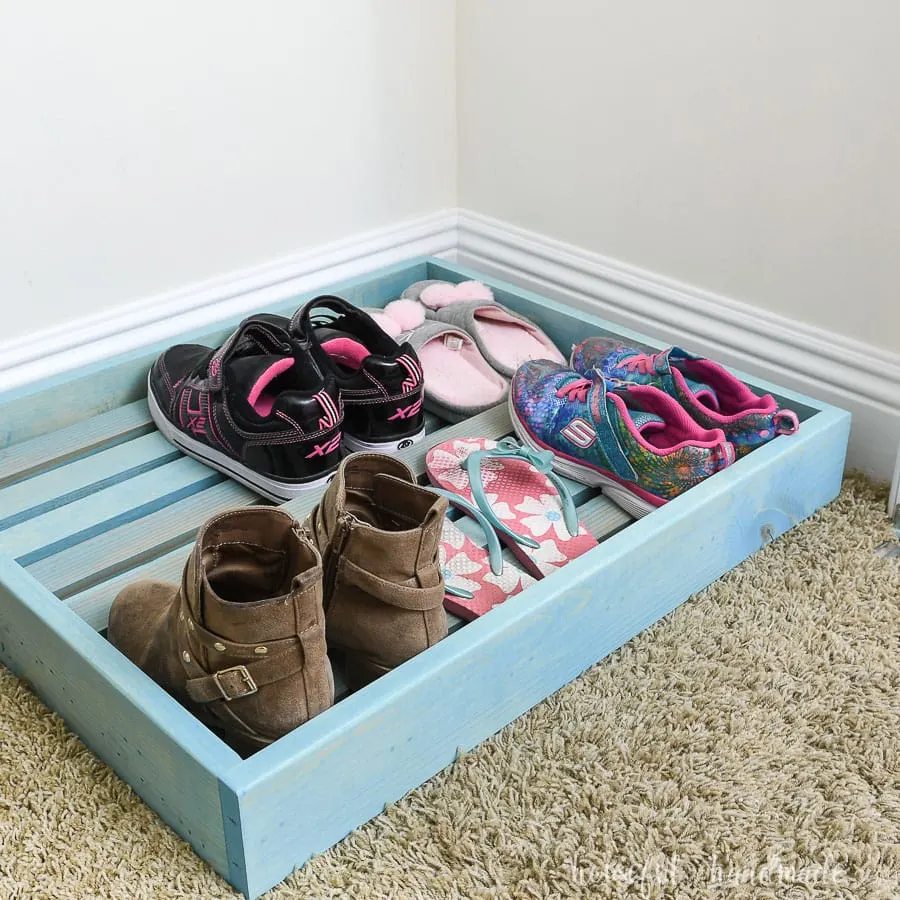 Turquoise stained shoe storage tray in the bottom of a kids closet.
