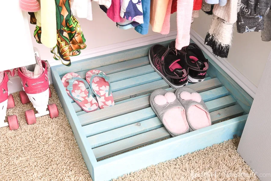 Shoe rack in the bottom of the closet with shoes and slippers on it. 