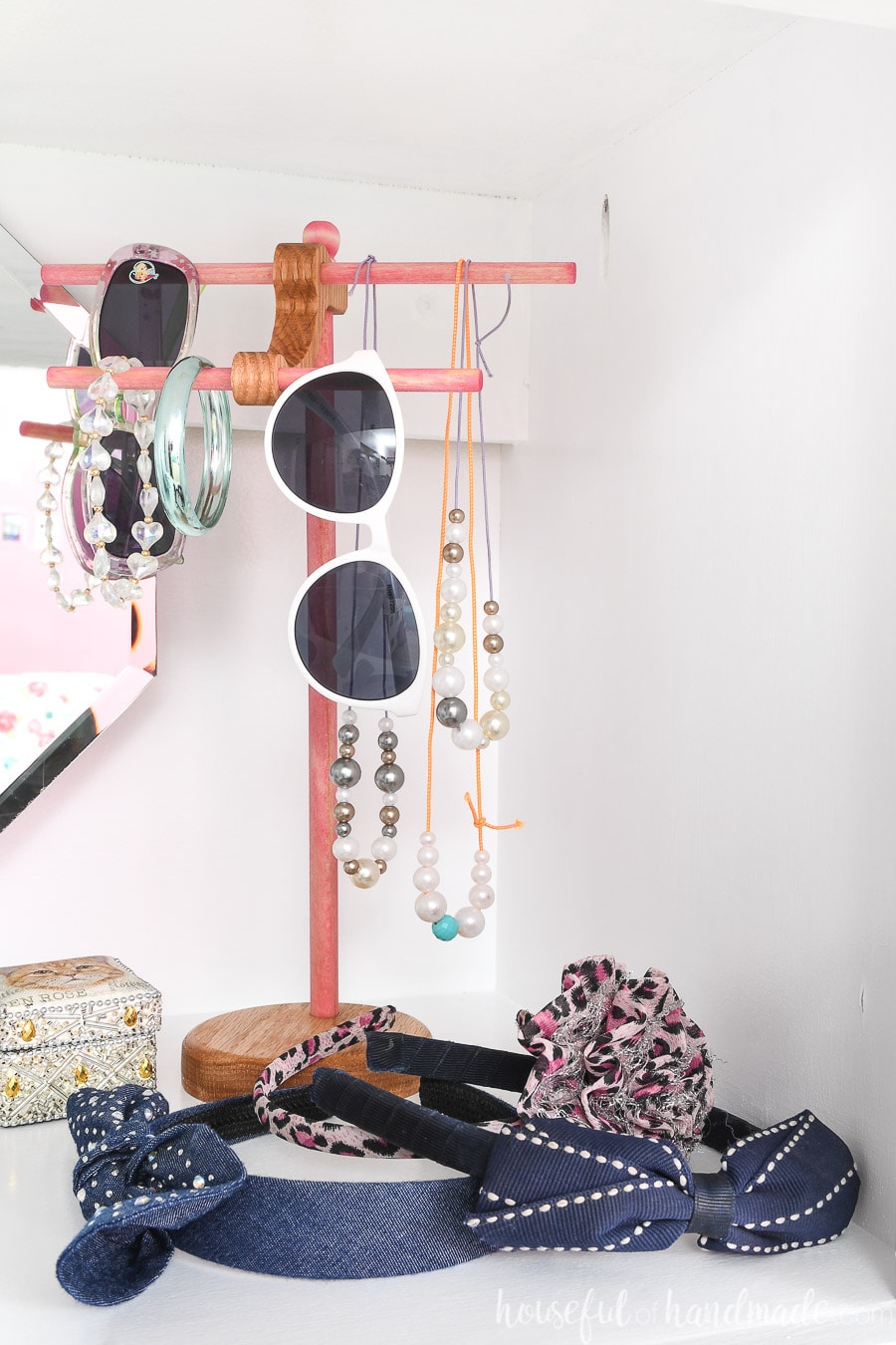 Wooden jewelry stand with kids bracelets, necklaces and sunglasses hanging on it.