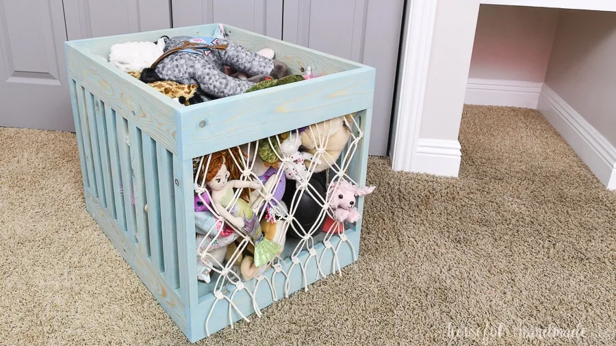 Macrame toy bin full of stuffed animals pulled out of the shelf nook.
