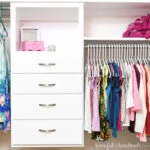 White DIY closet organizer with drawers inside a children's closet with clothes handing around it.