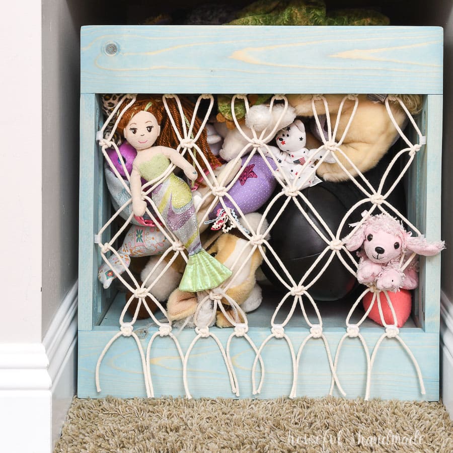 Macrame net on the front of a wooden crate to hold stuffed animals.