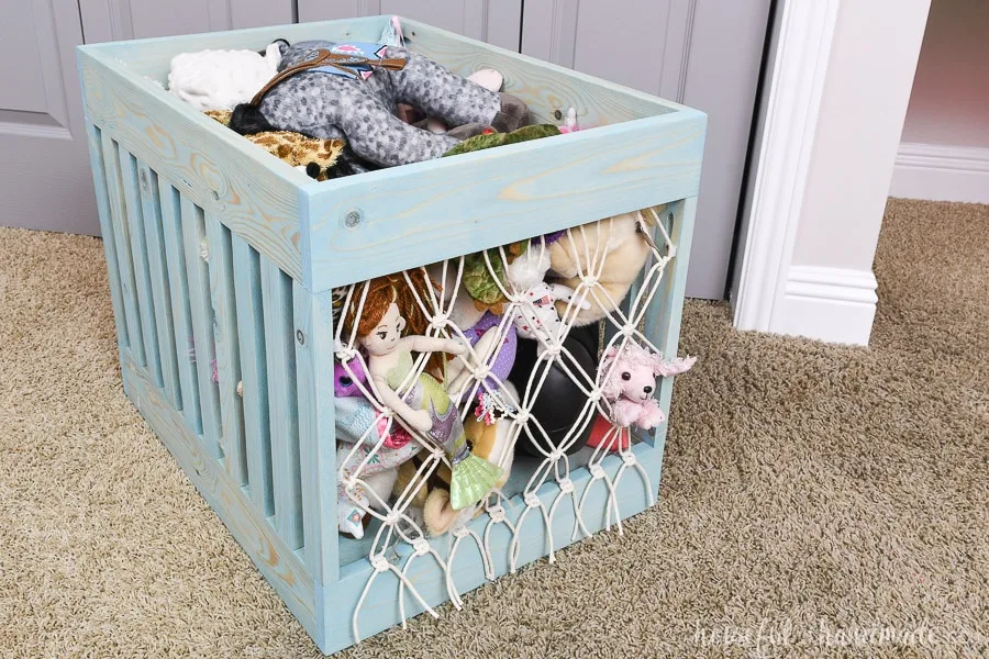 Full view of the wooden toy bin with macrame netting on the front and back in front of the closet.