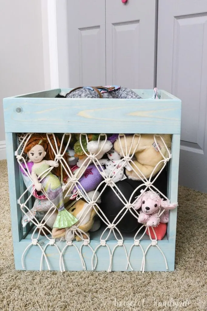 DIY stuffed animal storage made from turquoise stained wood with a macrame tied net on the front and back. 