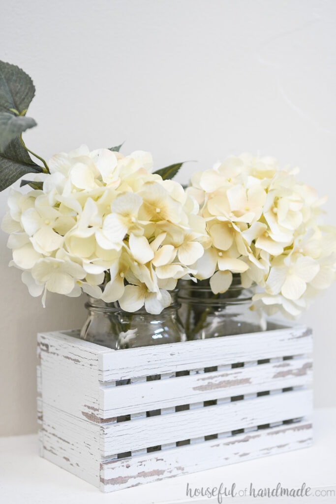 White hydrangea inside quart mason jars in a decorative farmhouse trough.