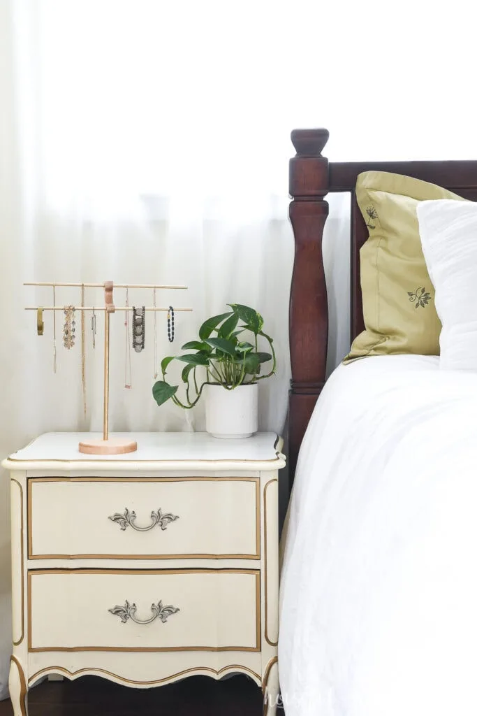 Bedroom nightstand with brass and wood necklace holder and potted plant on it.