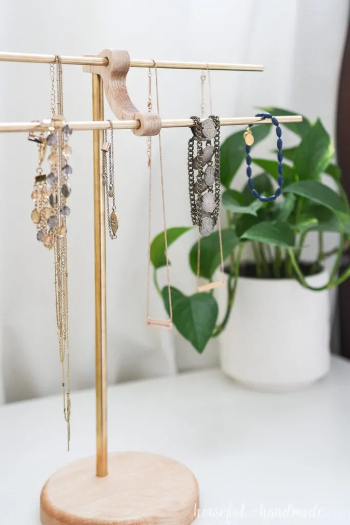 DIY necklace holder made with maple wood and brass rods on nightstand.