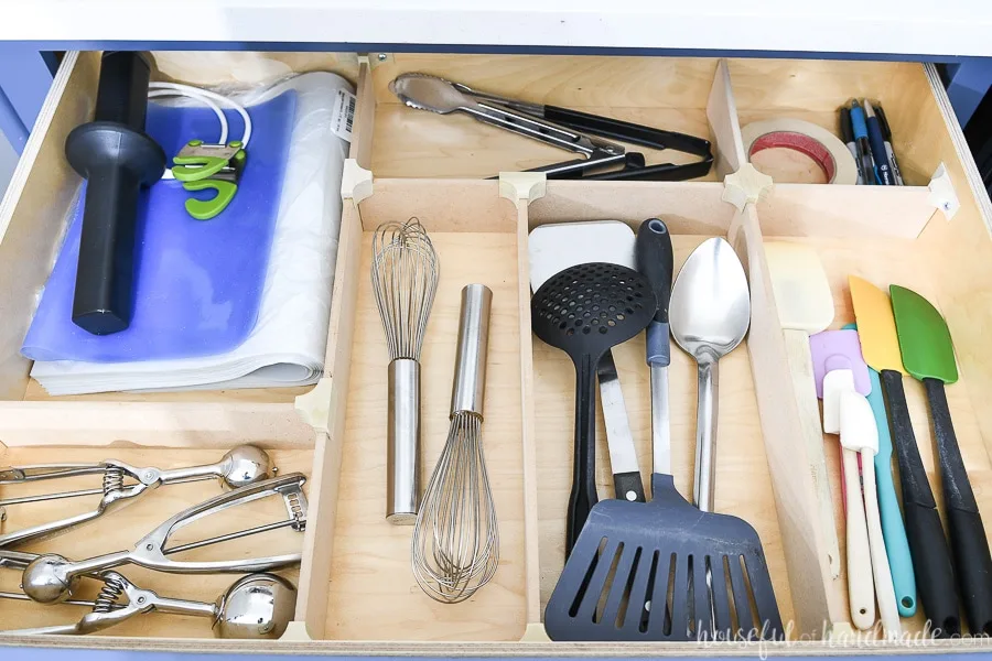 Organized drawer with kitchen utensils in it, separated by wood drawer dividers. 