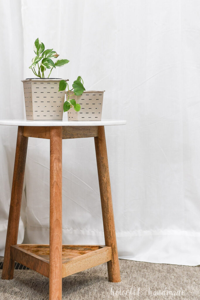 Two rose gold painted flower pots holding house plants on top of an end table.