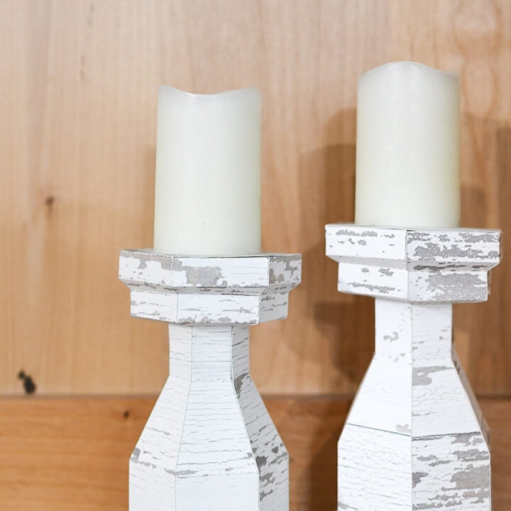 Two chunky candlesticks with chippy white paint texture in a bookcase.
