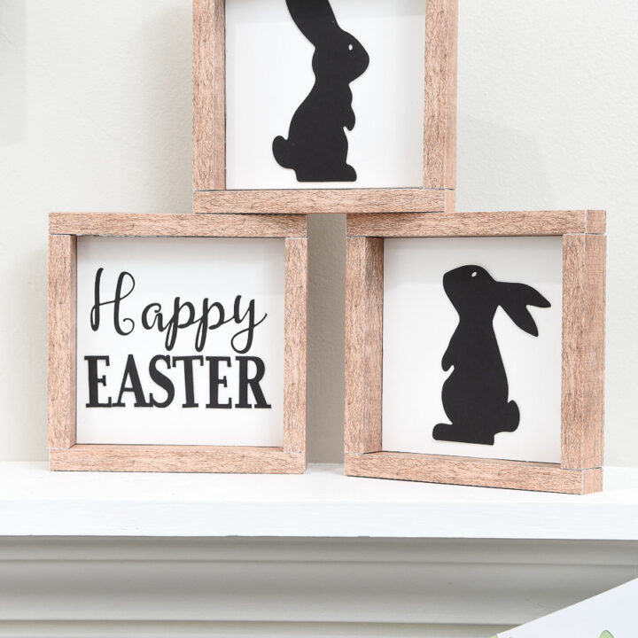 Three farmhouse Easter signs stacked in a pyramid on a shelf.