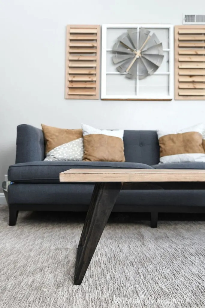 Coffee table with black legs and natural wood top in front of a sofa with pillows. 