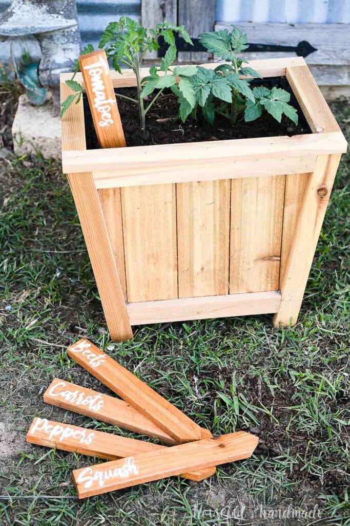 Five homemade wood garden markers, one in the planter next to plants.