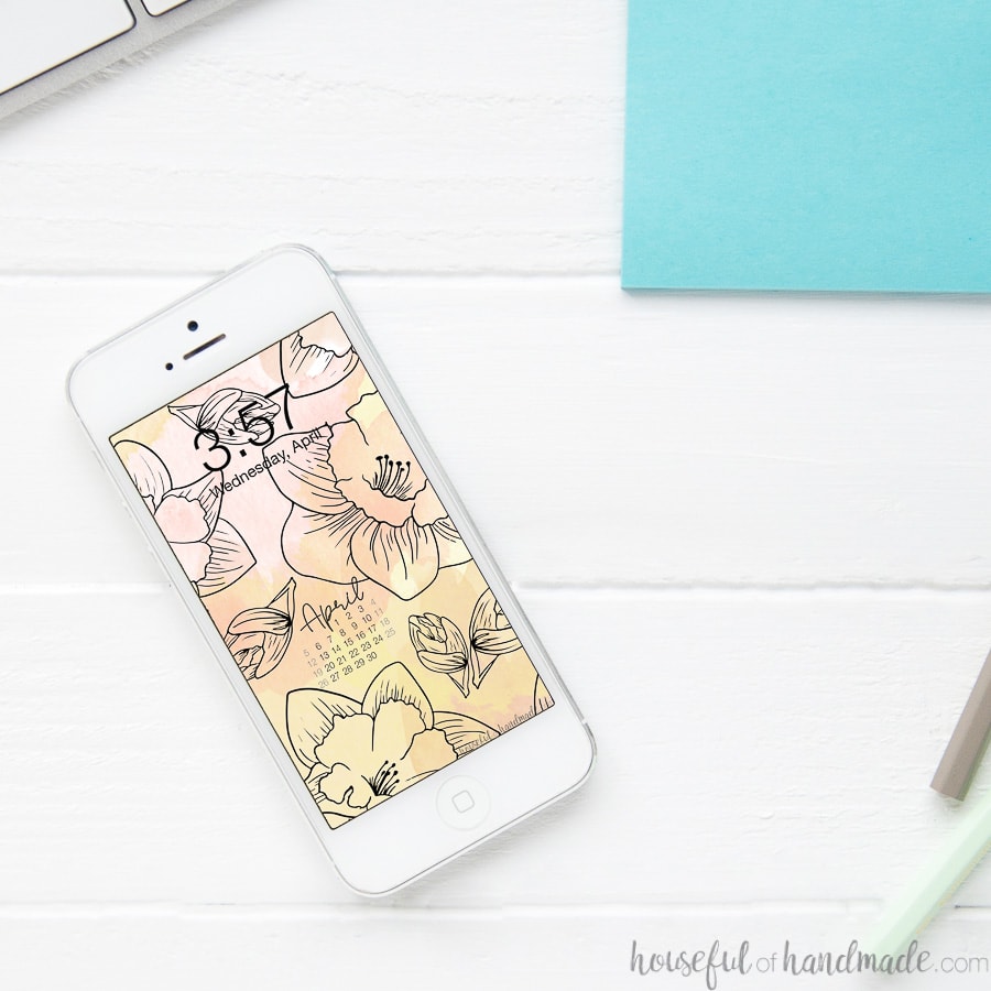 Smartphone sitting on a white desk with free digital wallpaper on the screen.