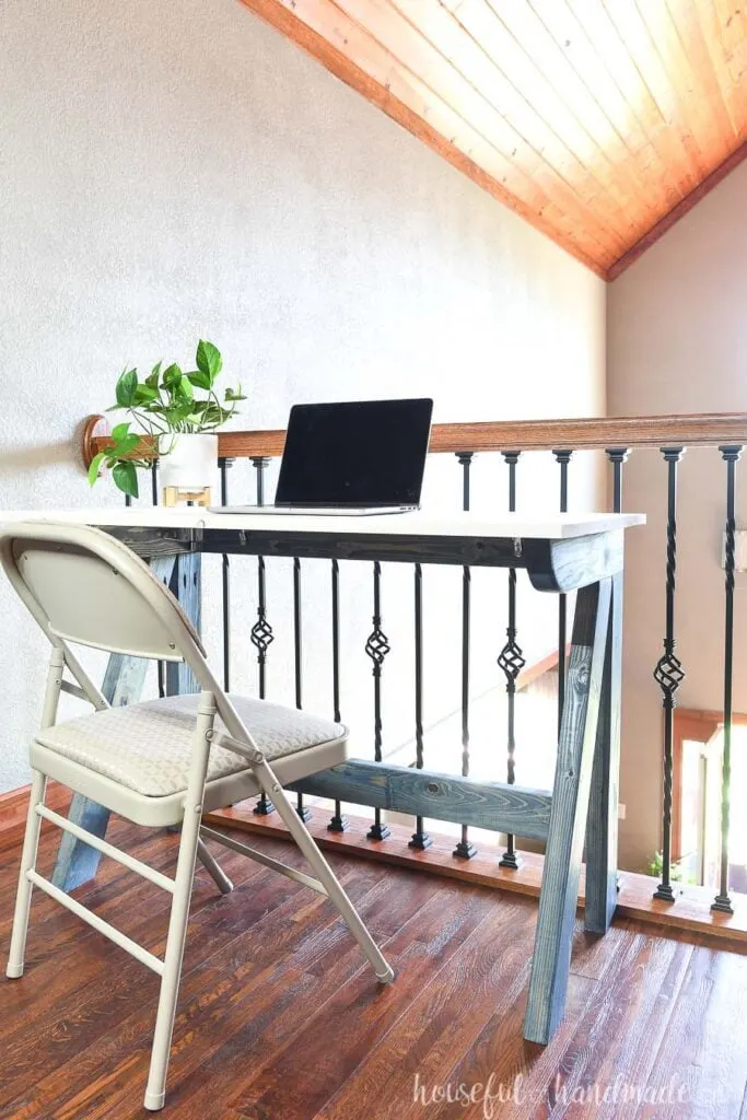 Blue and white desk made from 2x4s sitting in the loft area with a laptop on it. 