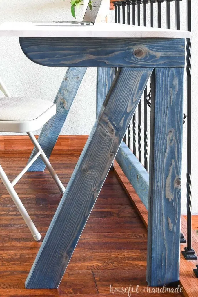 Close-up view of the fold-away desk base made from 2x4s and stained navy blue.