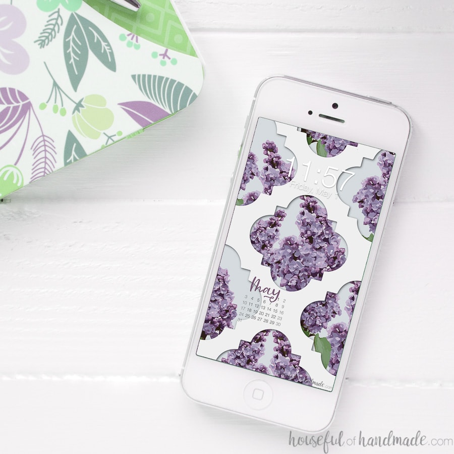 Lilac design digital wallpaper on the background of a white iPhone sitting on a table.
