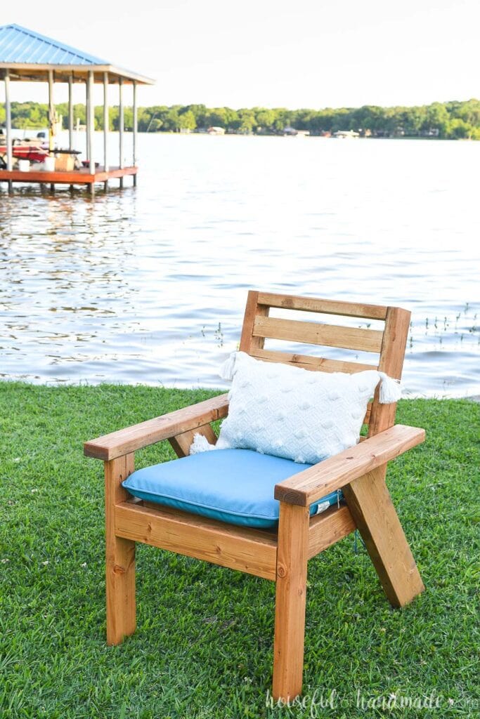 Outdoor lounge chair with turquoise cushion and white pillow on the grass in front of a lake. 
