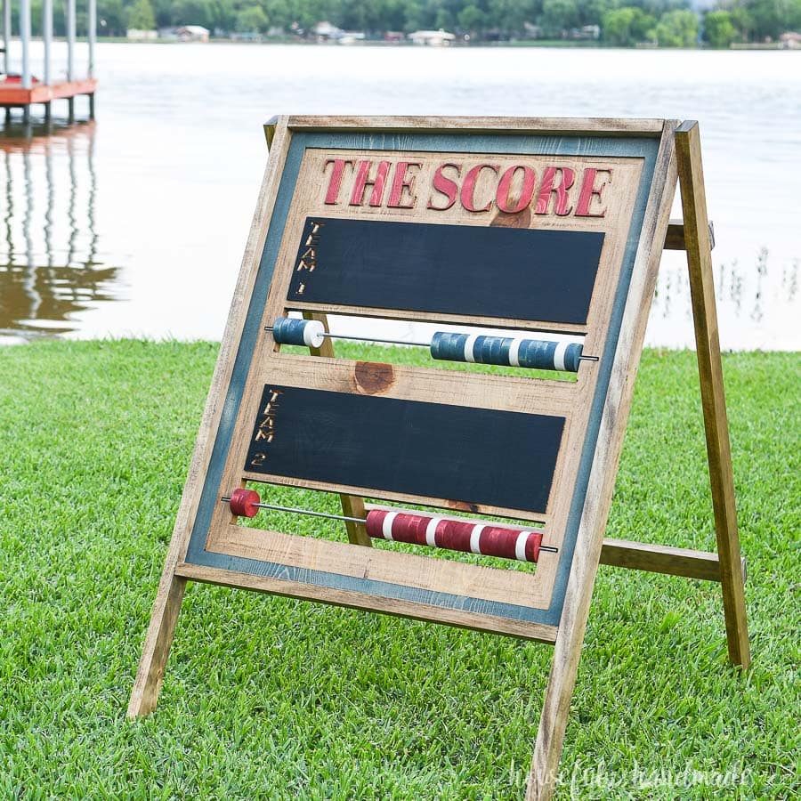 Square photo of the carved scoreboard with red and blue wood beads sitting on the grass.