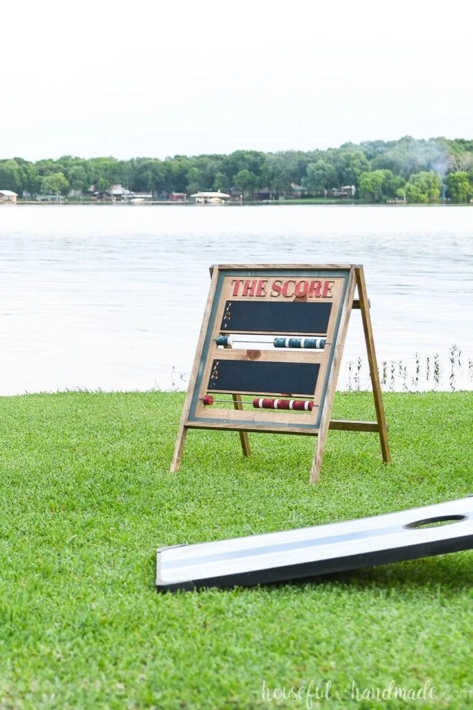 DIY scoreboard on the lawn in front of the lake with corn hole board in front of it.