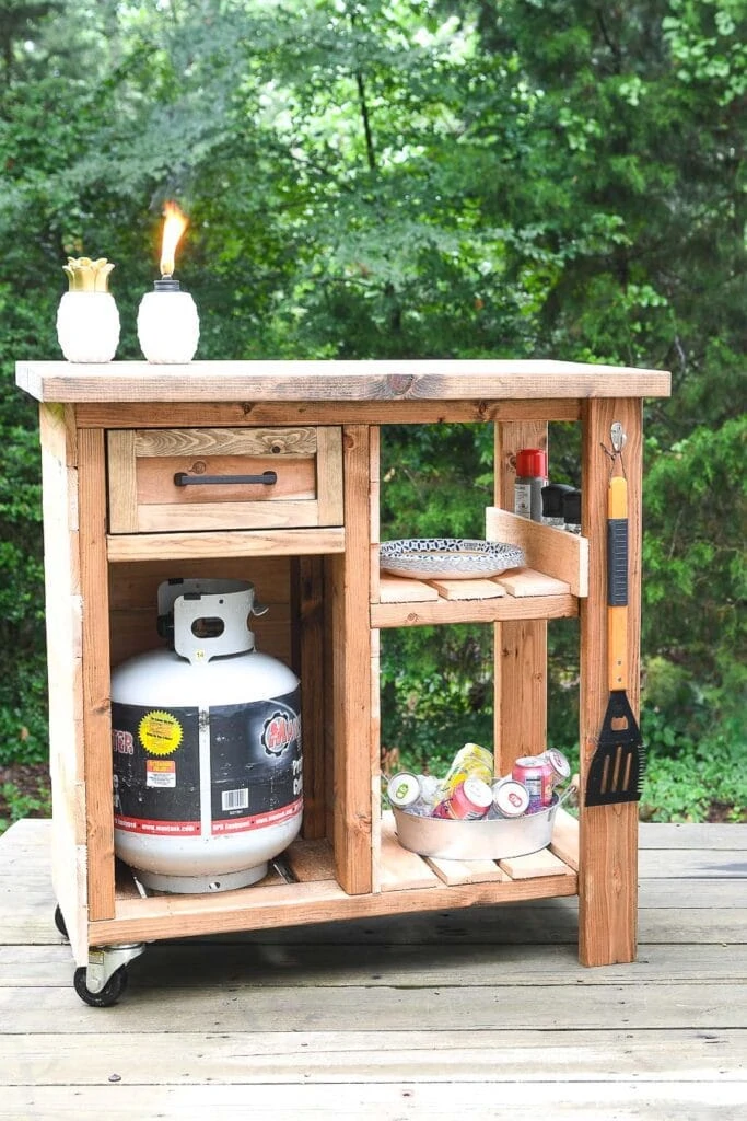 Outdoor grill table on wheels with cedar slats on the sides and on the shelves. 