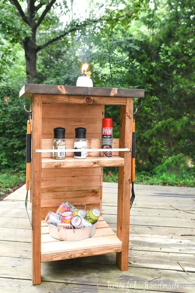 Grill cart with spice rack on the end holding salt & pepper grinders and gilling spray, bottom shelf with drinks in a bucket. 