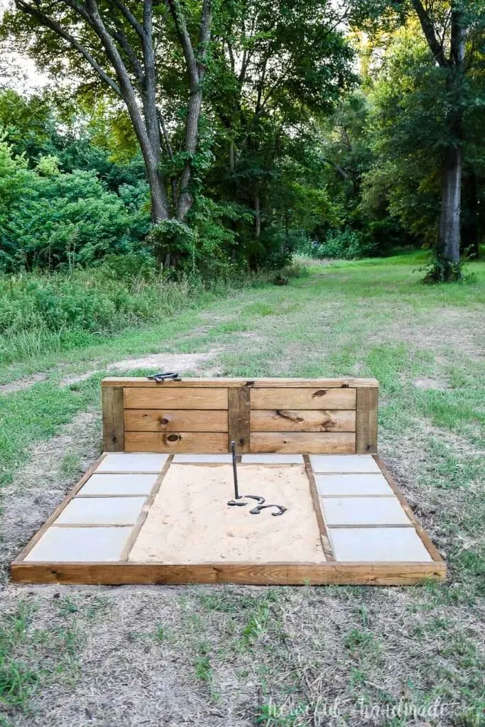 Straight on view of one of the horseshoe pit frames installed in the lawn with 2 horseshoes in the pit by the stake. 