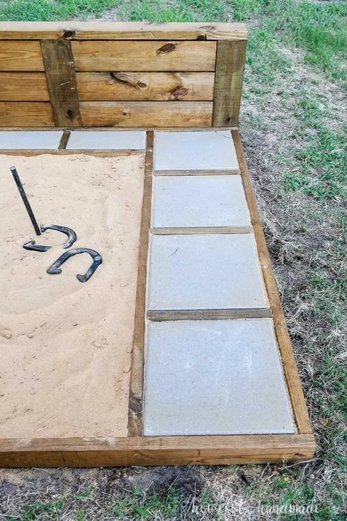 A looks at the right side of the ultimate DIY horseshoe pit stained walnut with gray pavers in the frame. 