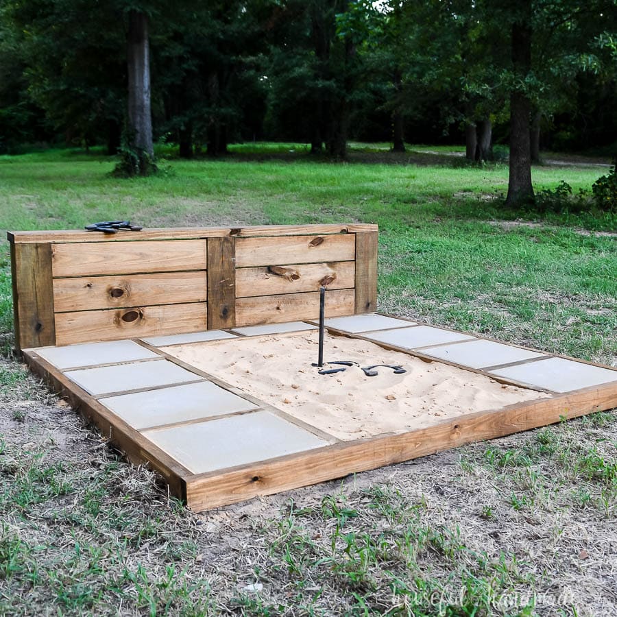 DIY Horseshoe pit with sturdy backstop and throwing platforms with concrete pavers.