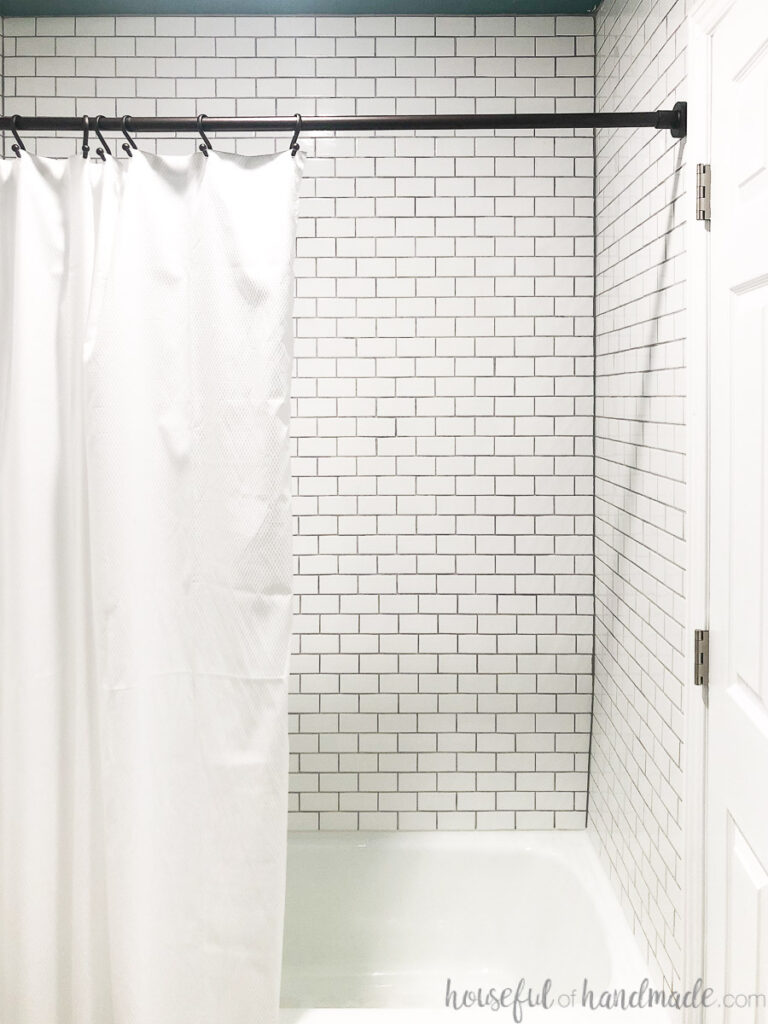 Shower tiled with small white ceramic subways tiles and rubbed bronze shower curtain rod with white shower curtain. 