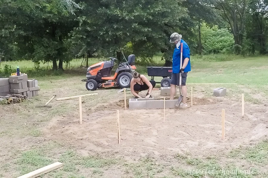 Leveling the first row of cinder blocks and cinder block caps for the base of the fire pit for the first of the hexagon. 