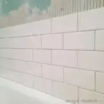 Five rows of white subway tiles starting to be installed above a bathtub.