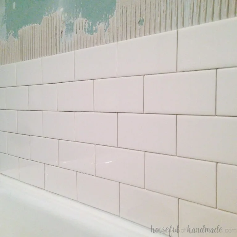 Five rows of white subway tiles starting to be installed above a bathtub.