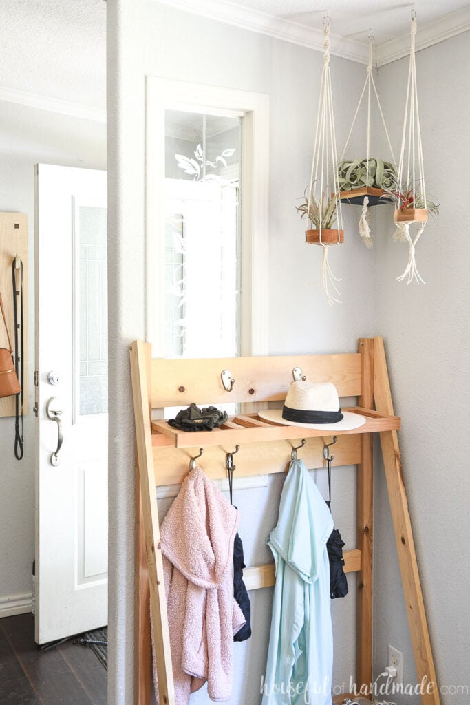 Entryway with three hanging air plants in the corner above the folding mudroom storage shelves. 