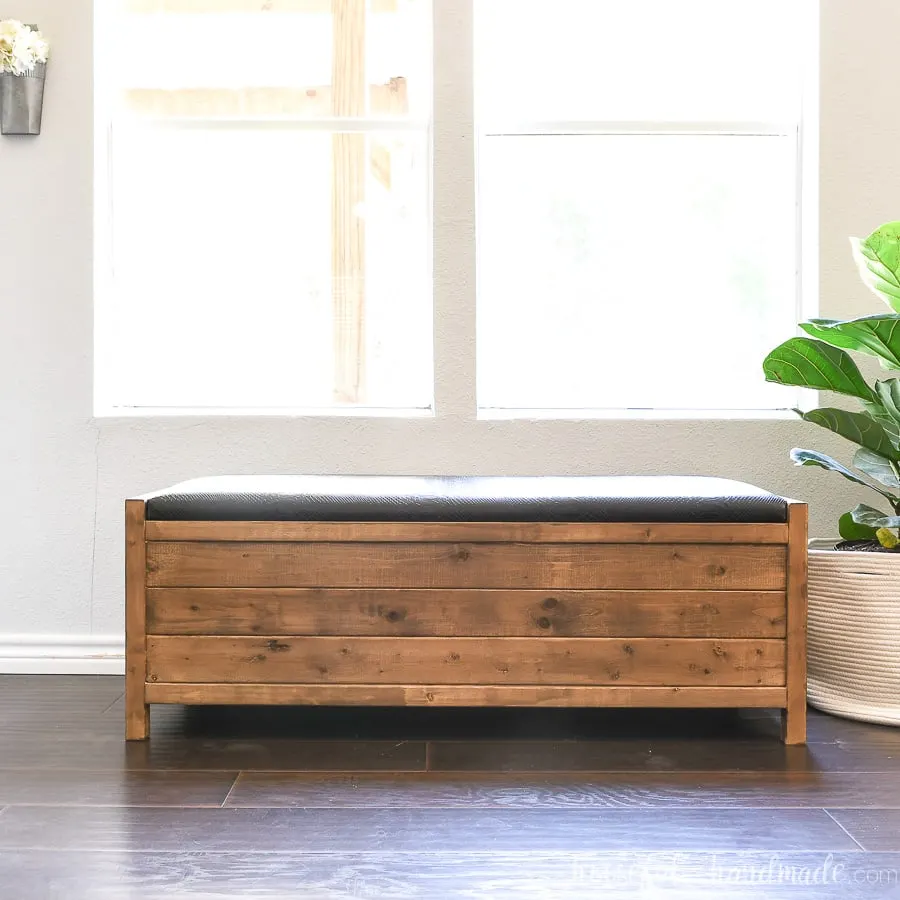 DIY storage bench with upholstered top and large storage compartment in front of a window.