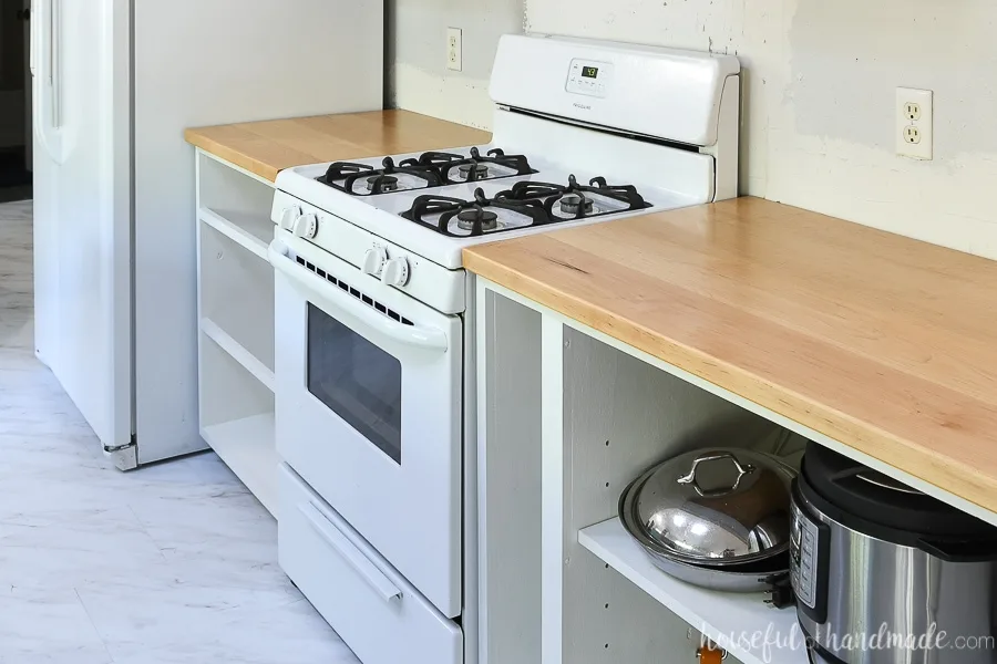 White cabinets carcasses installed around white range with light colored wood countertops on them.