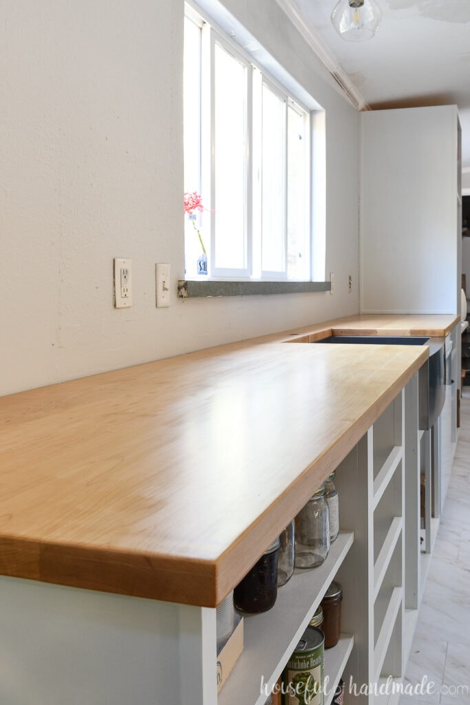 Bank of white cabinets without doors/drawer fronts, sitting in front of a window, with a light wood countertop installed on top. 