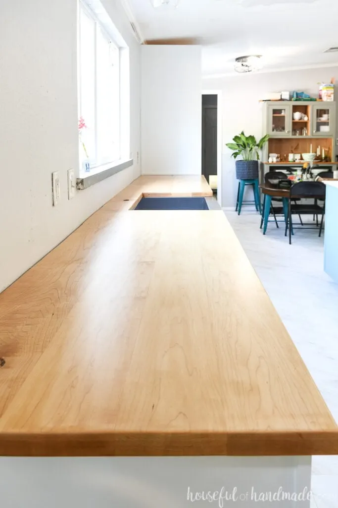 Looking down the length of the long wood countertop in the kitchen with a cut out for a farmhouse sink seeing the dining room in the background.