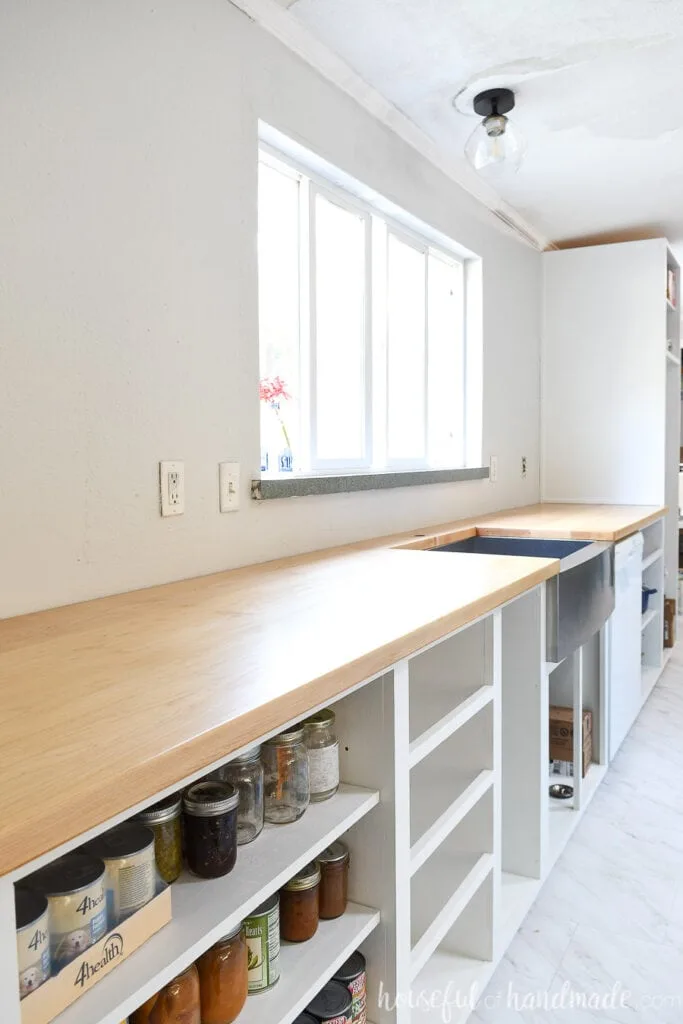 Long wall of base cabinets with a DIY hardwood countertop and stainless steel apron front sink in front of a large window. 