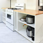 White cabinets around the stove with solid wood countertops sealed with a matte finish on them.