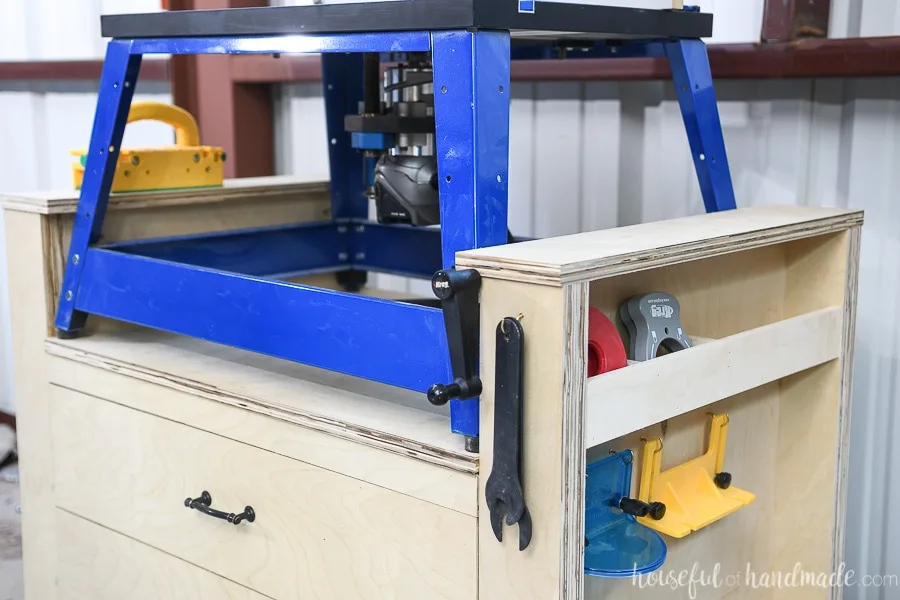 The right side of the router table with a spot under the raised side ledge holding the crank for the router lift and a hook holding the wrenches. 