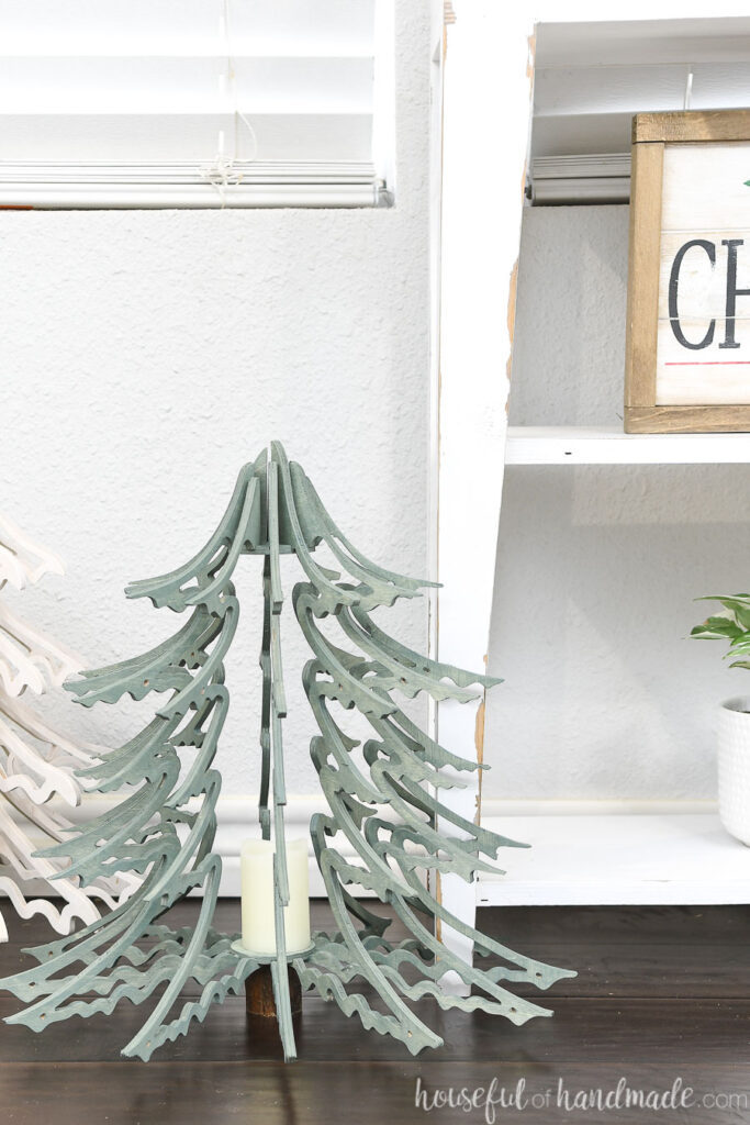 Close up of the Blue Spruce inspired wood Christmas tree lantern sitting on the floor by a white console table. 