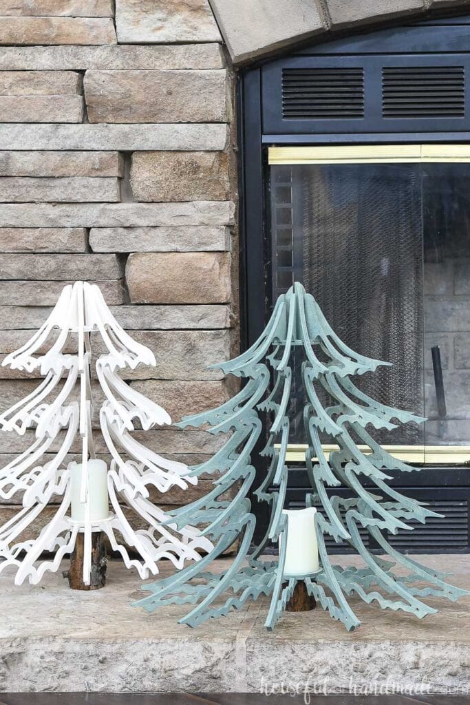 The white and blue-green stained plywood Christmas trees sitting on a stone hearth. 