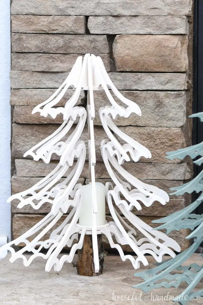Close up of the smaller, white stained 3D wood Christmas tree with drooping branches sitting on the hearth.