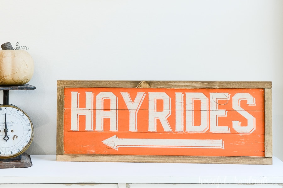 Orange and cream hayride wood sign with stained frame on a console table.