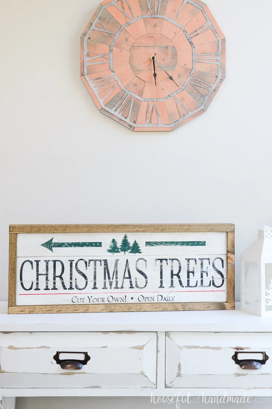 Christmas tree farm side of the double sided wood sign sitting on a white console table under a rustic wall clock. 
