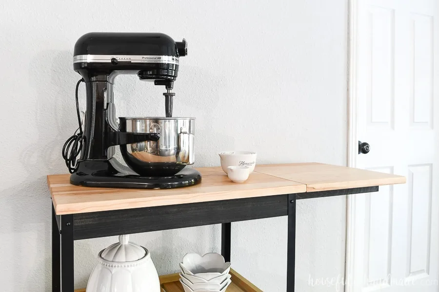 Close up view of the top of the kitchen cart with the drop-down leaf up next to a Kitchen aid mixer. 