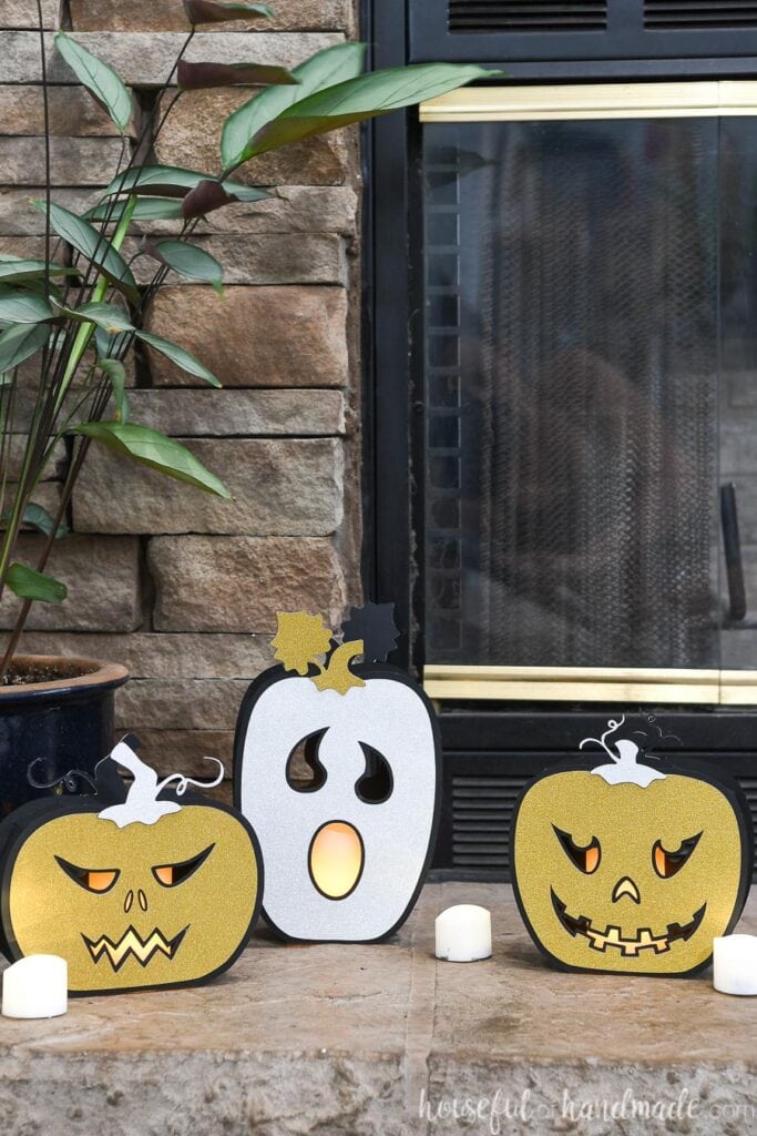Three Halloween pumpkin lanterns made from black and glitter cardstock, sitting in front of a fireplace. 
