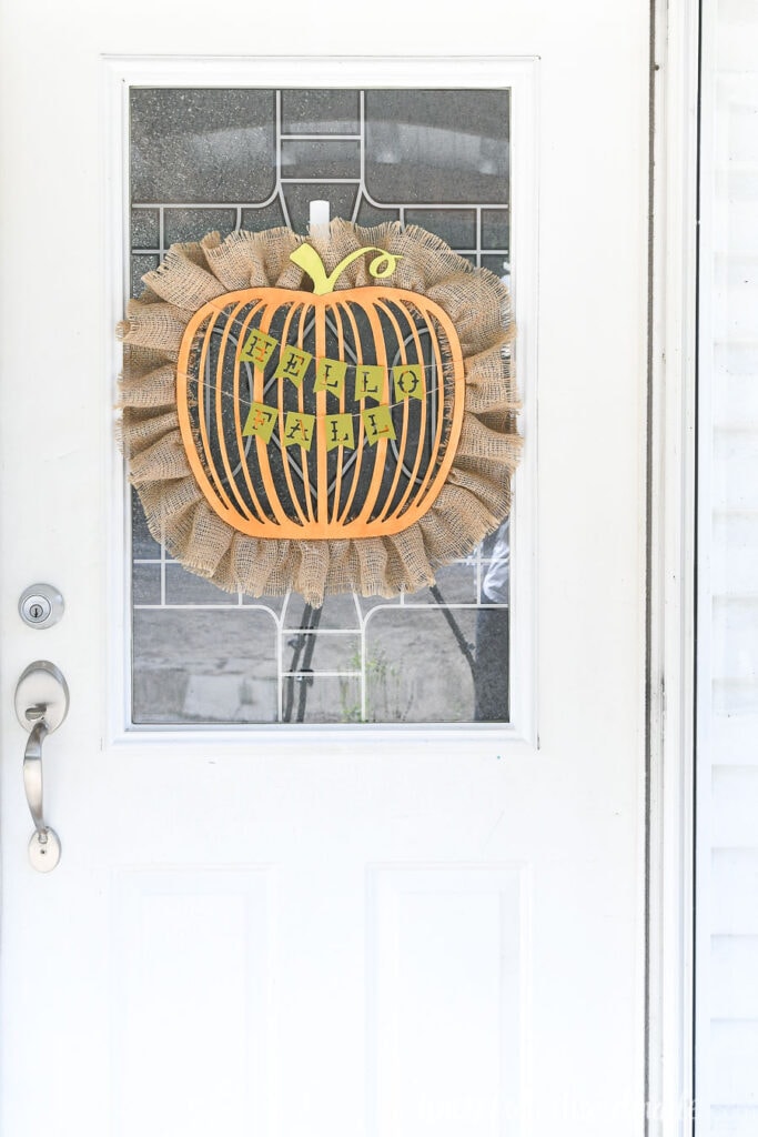 White front door with fall pumpkin wreath hanging over the window. 