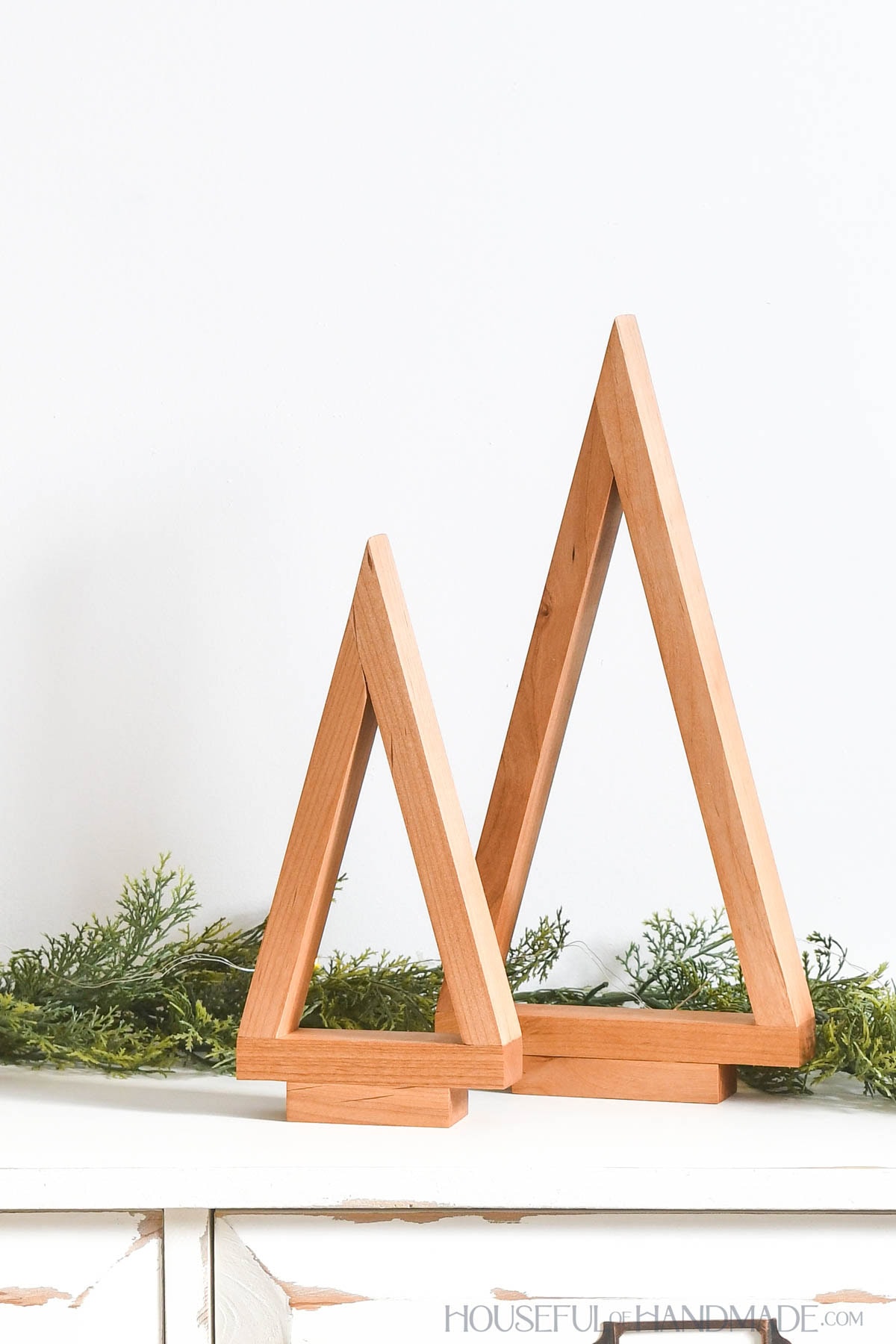 Two simple wood Christmas trees nestled on a table with garland. 
